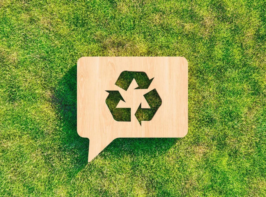 Símbolo ecológico de reciclaje tallado en madera reciclada sobre césped verde